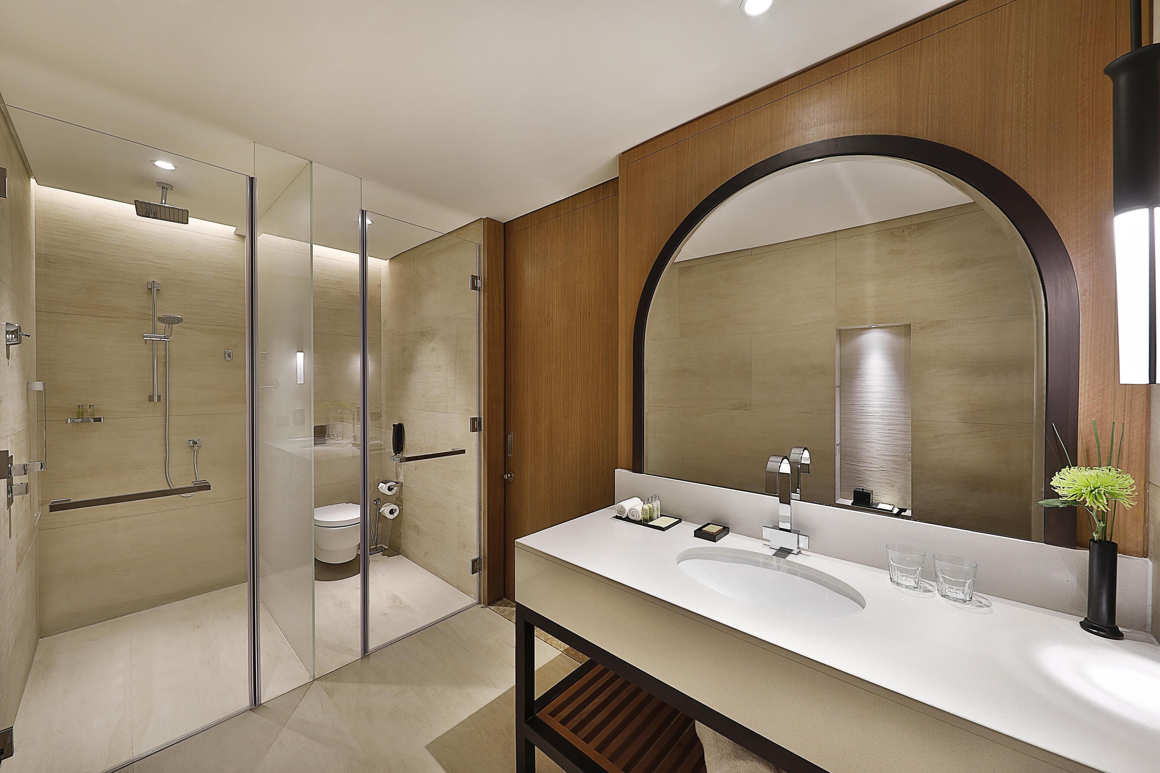 A modern bathroom with a glass-enclosed shower, a large mirror, and a white sink.