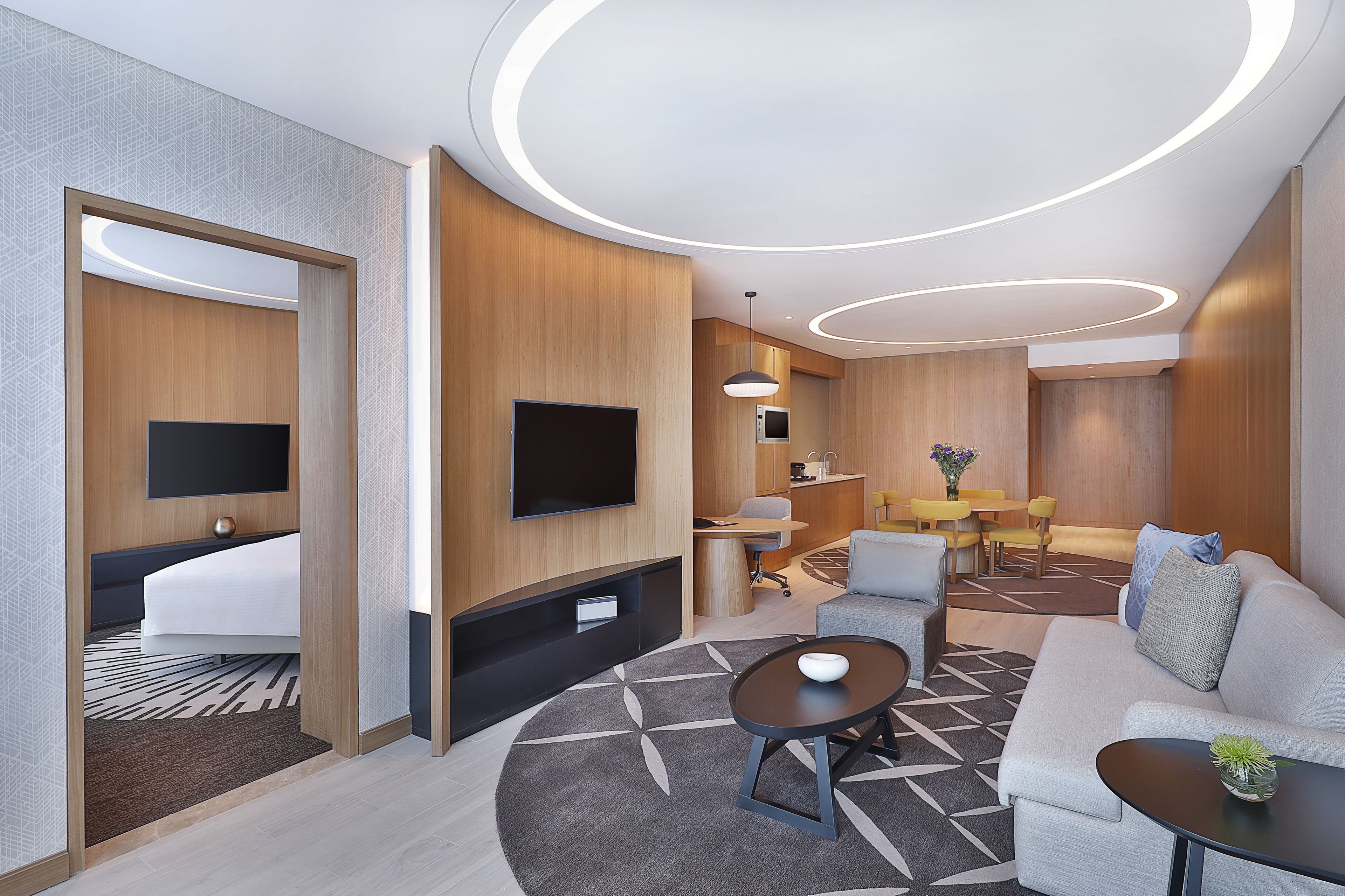A modern hotel room with a sofa, a coffee table, a TV, a desk, and a dining area.