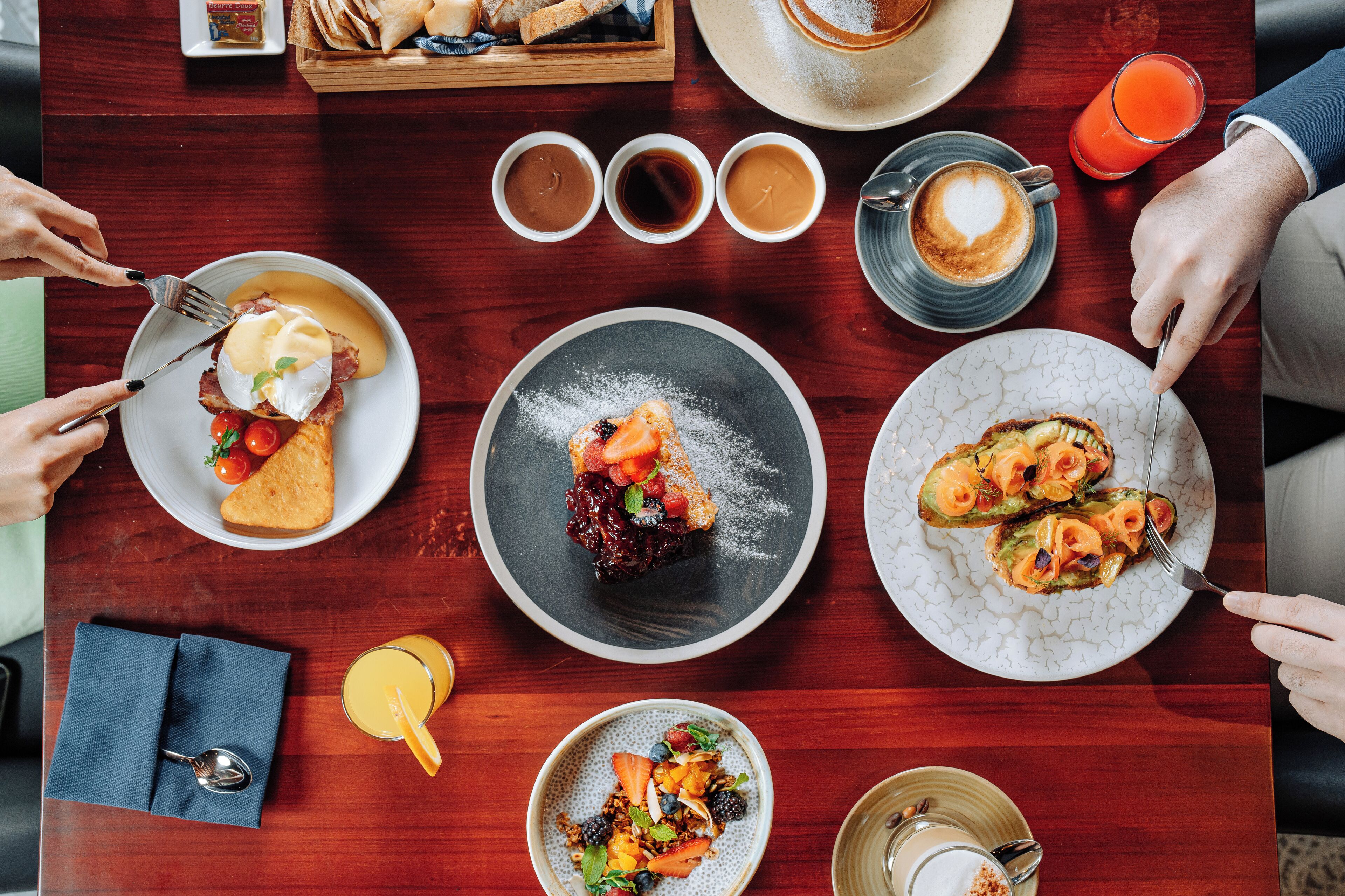 Una mesa de comedor con diversos platos, tazas de café y un vaso de jugo de naranja.