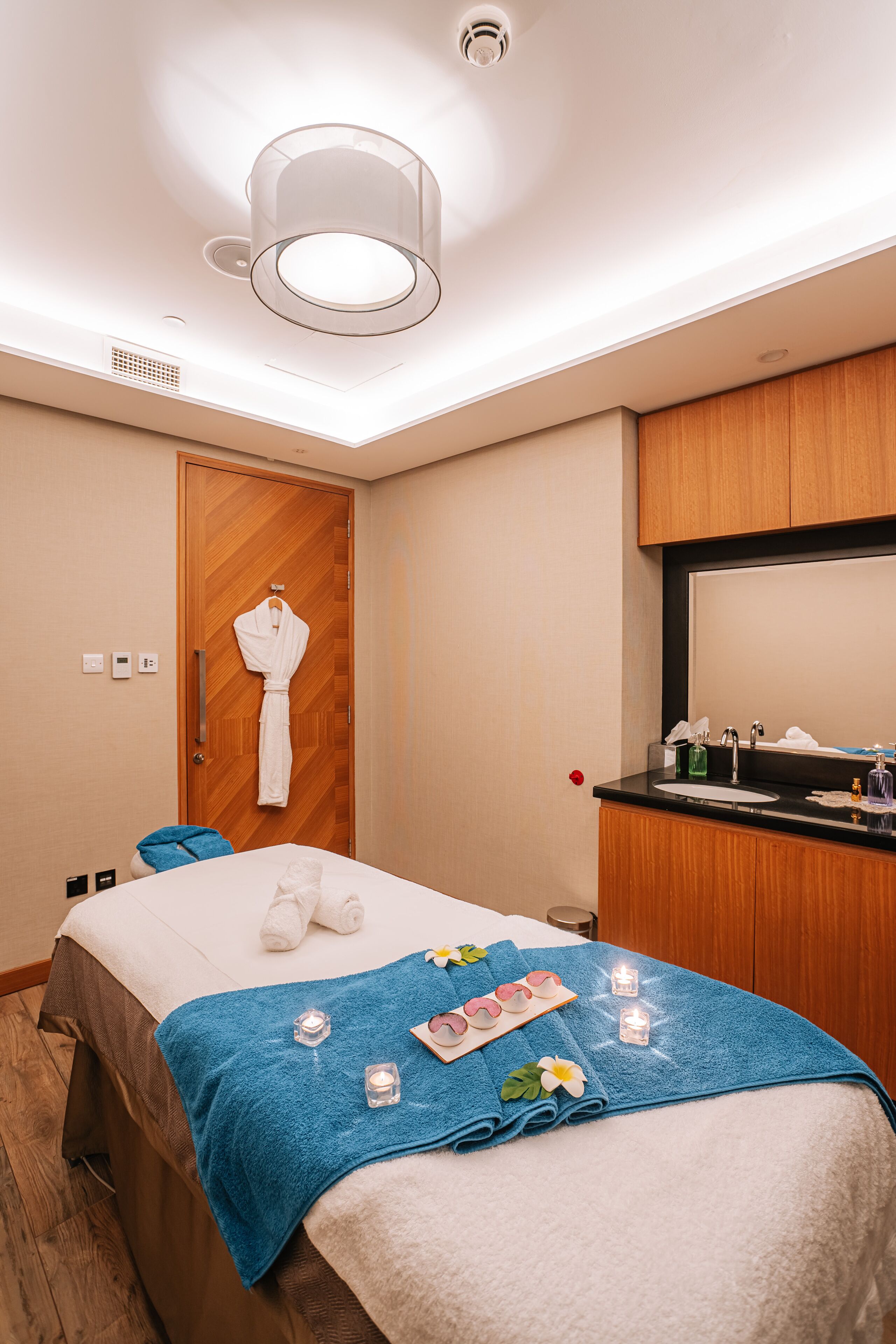 Habitación de hotel con cama, baño con lavamanos y espejo, y una bata colgada en la puerta.