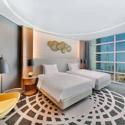 Two single beds with white linens, a comfortable armchair, and a city view.