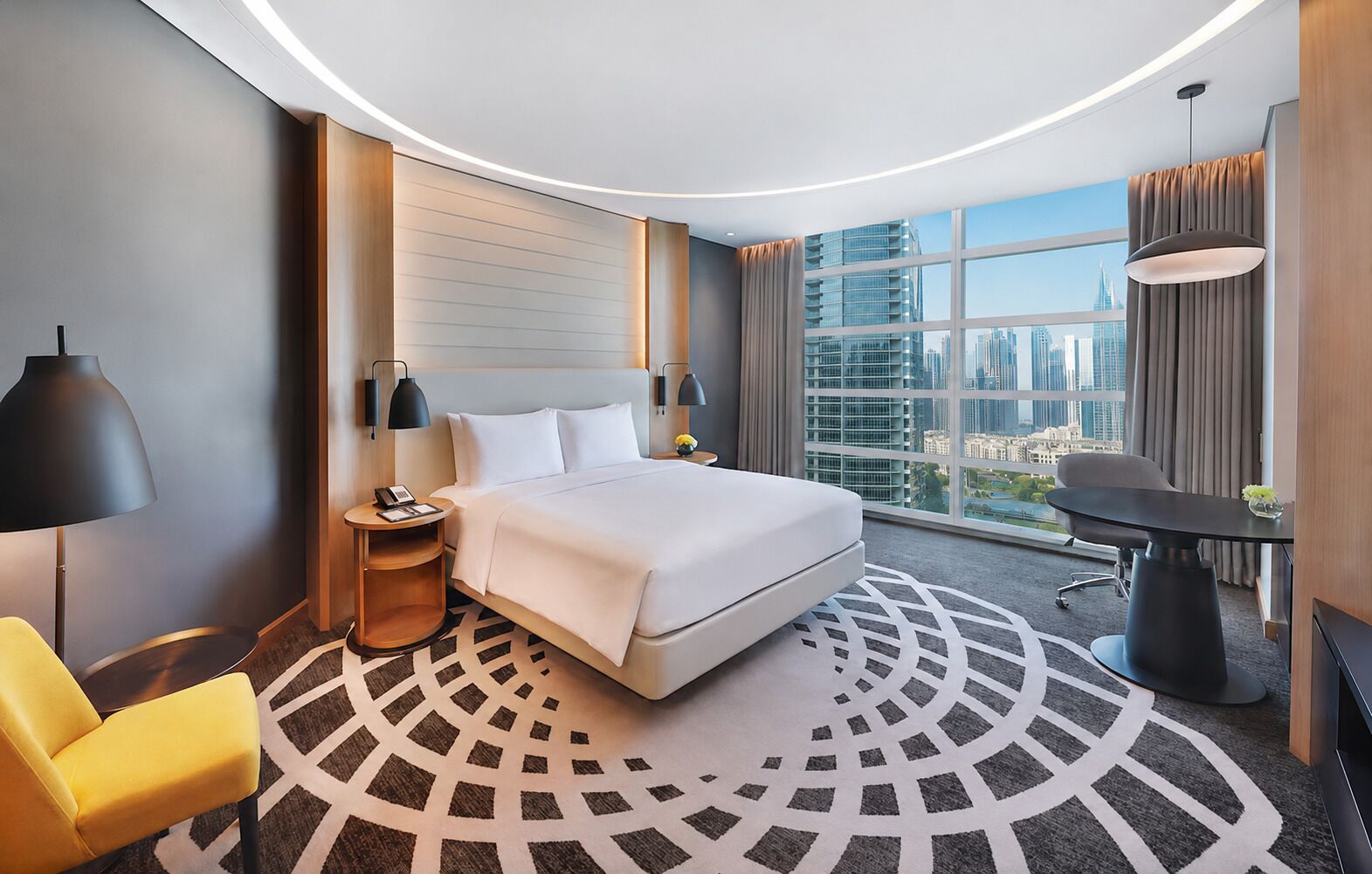 Une chambre d’hôtel moderne, dotée d’un grand lit, d’un bureau, d’une chaise et offrant une vue sur le paysage urbain.