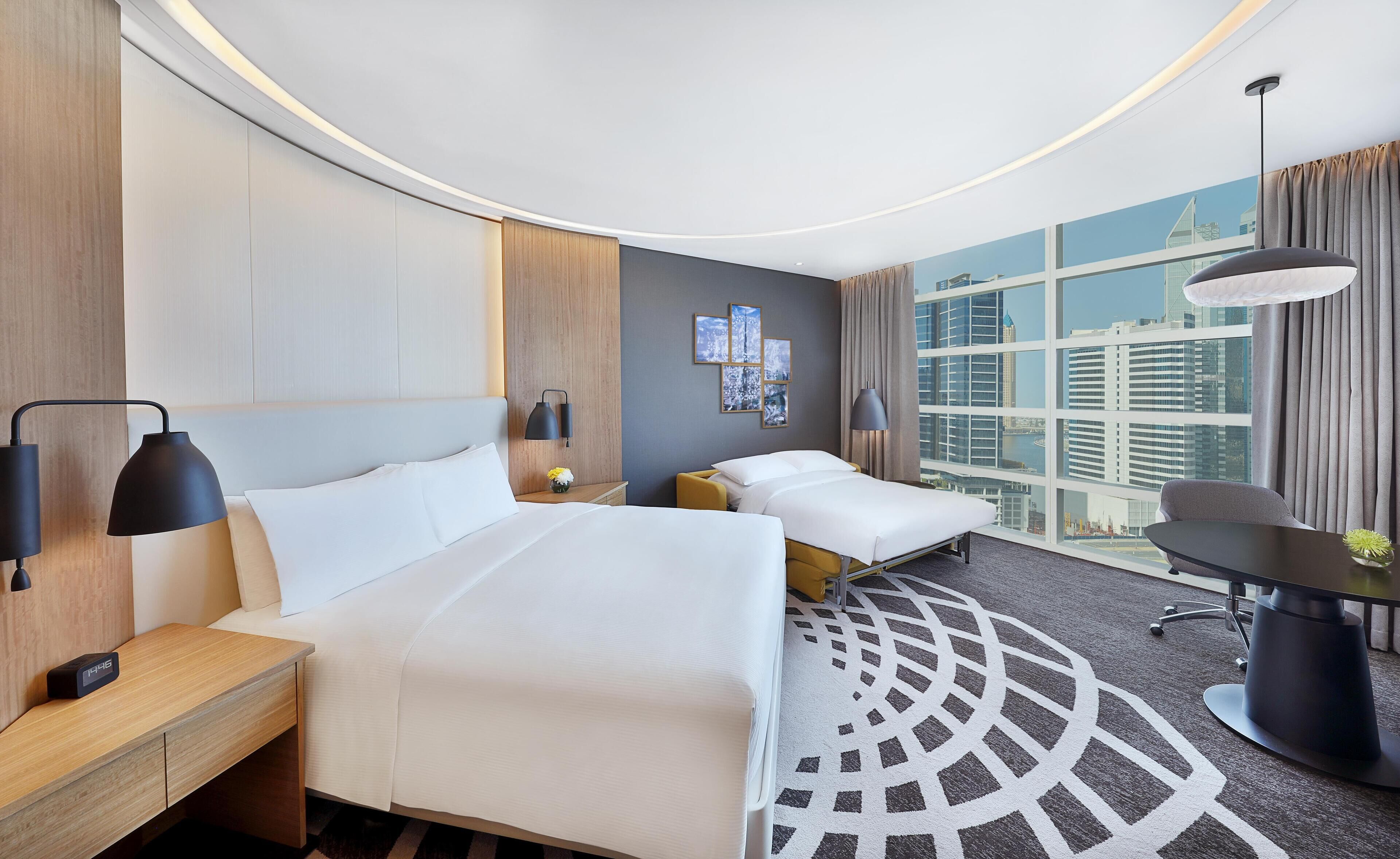 Une chambre d’hôtel avec deux lits, un bureau et une vue sur le paysage urbain.
