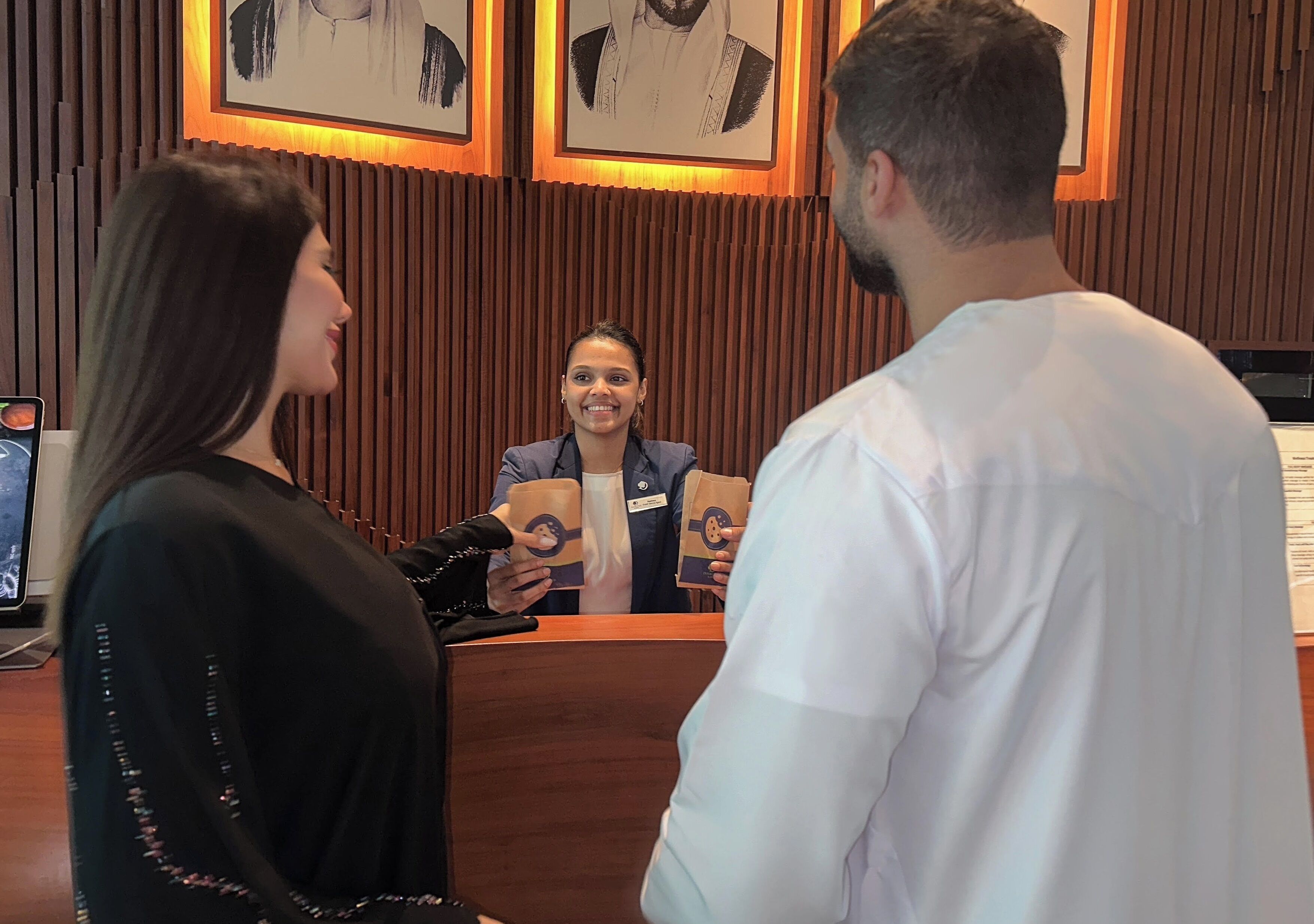 A reception desk with framed artwork on the wall, a wooden panel design, and a digital screen displaying a menu.