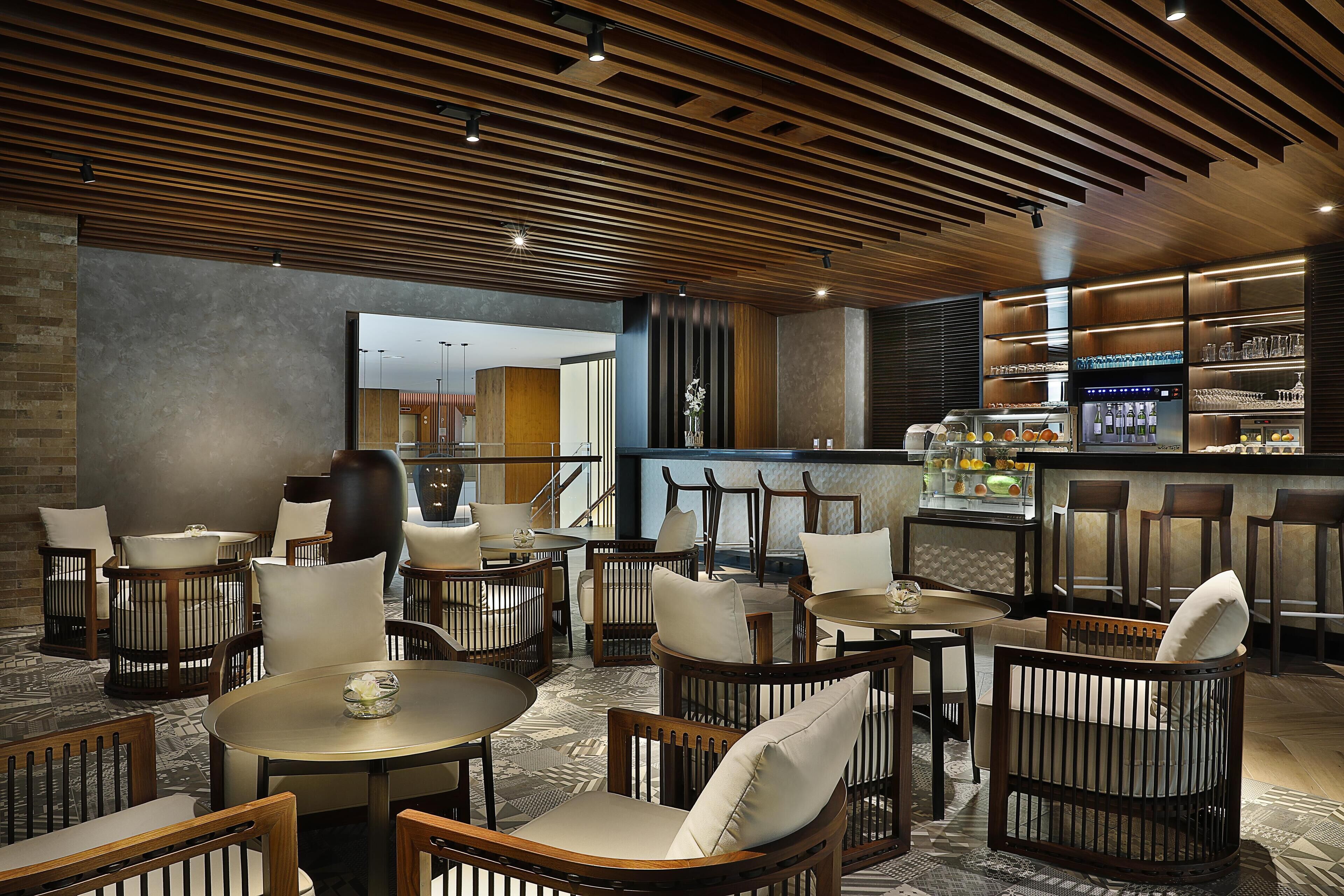 A modern restaurant with wooden furniture, a bar area, and a view into the kitchen.