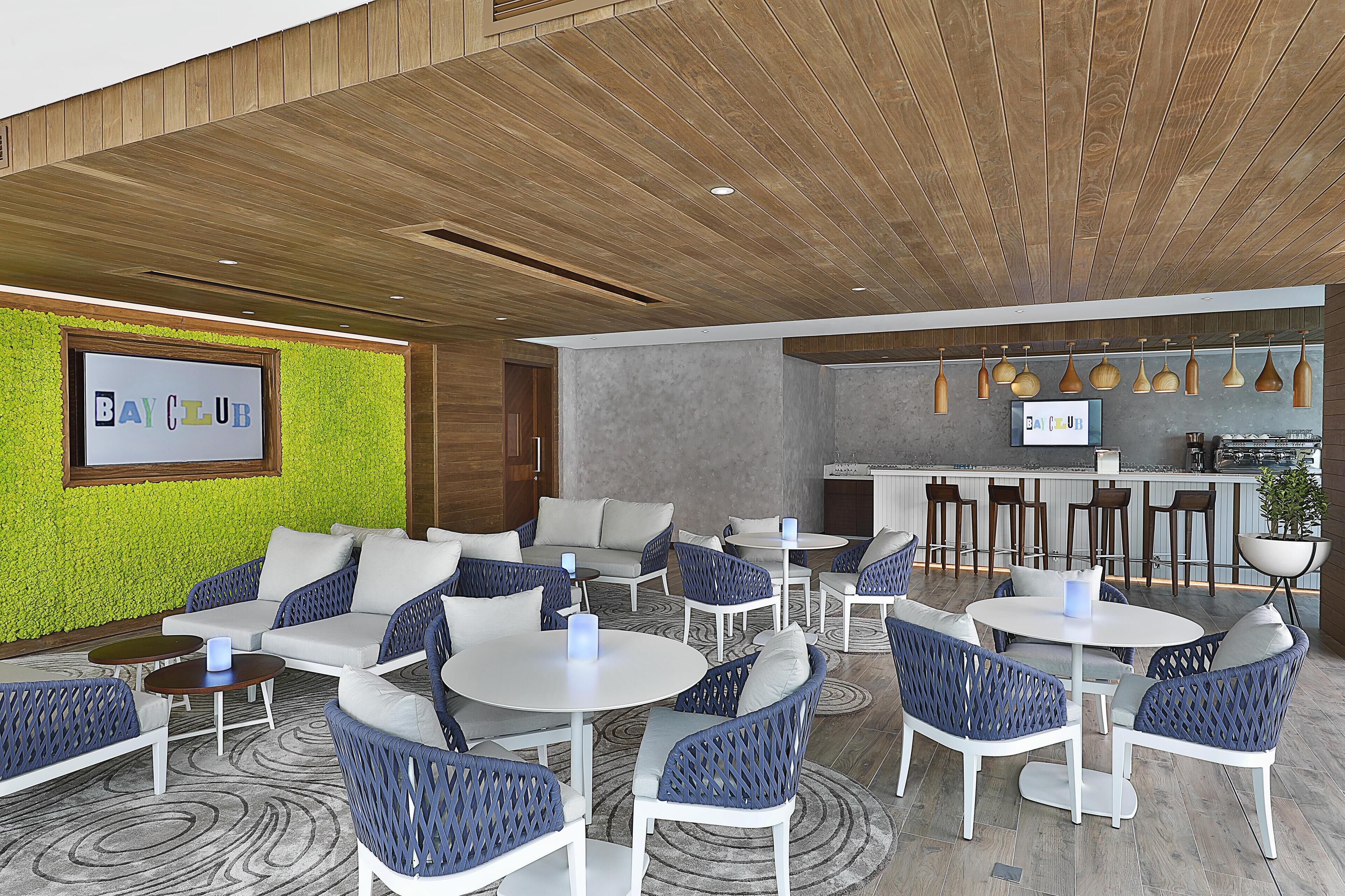 A modern lounge area with seating arrangements, a bar, and a green wall with a sign.