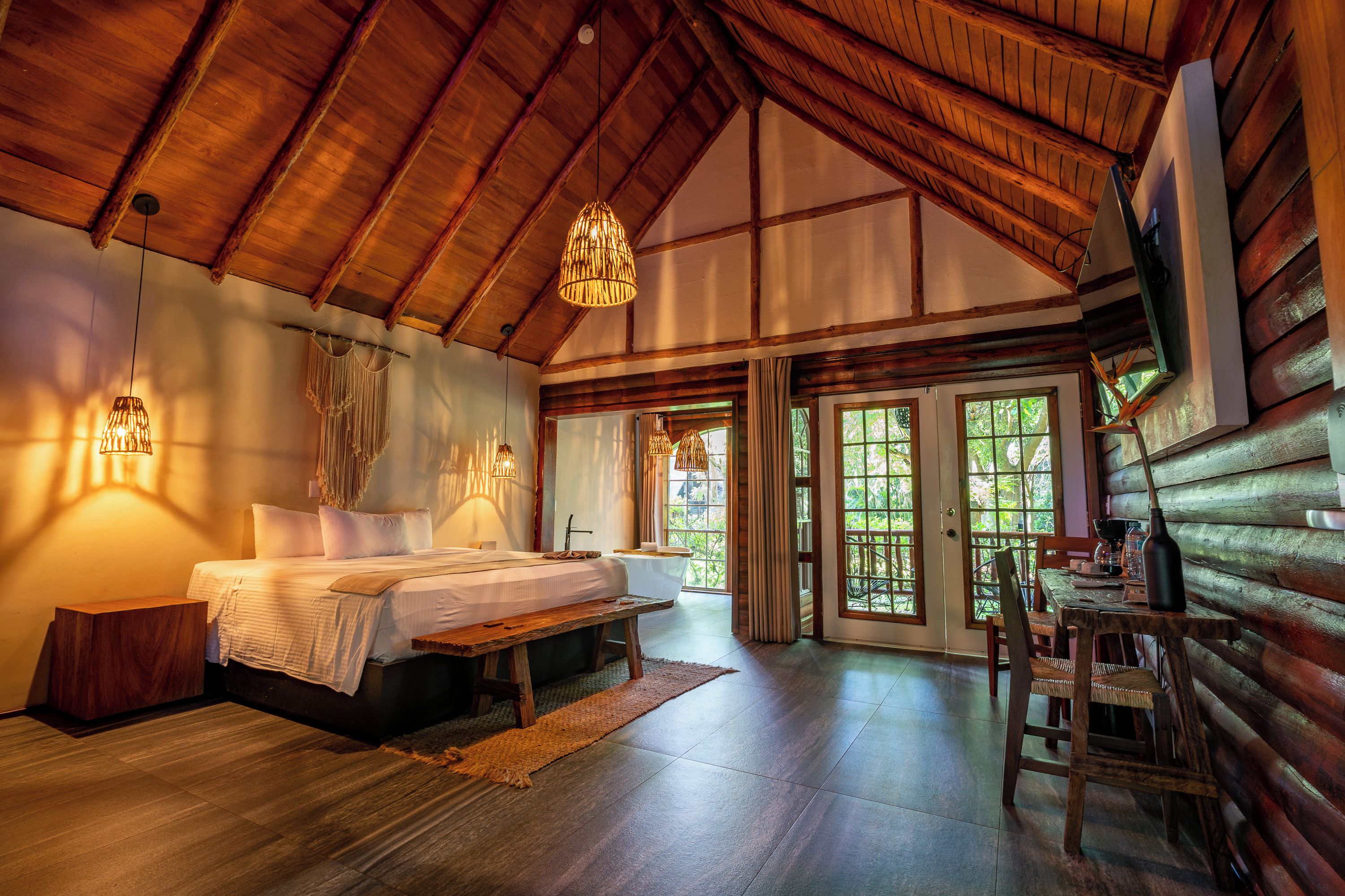 A log cabin interior with a bed, a table, and a view of the outdoors.