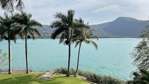 A landscaped area with palm trees and a view of a large body of water, likely a lake, with mountains in the background. - Santa María Resort (La Laguna)