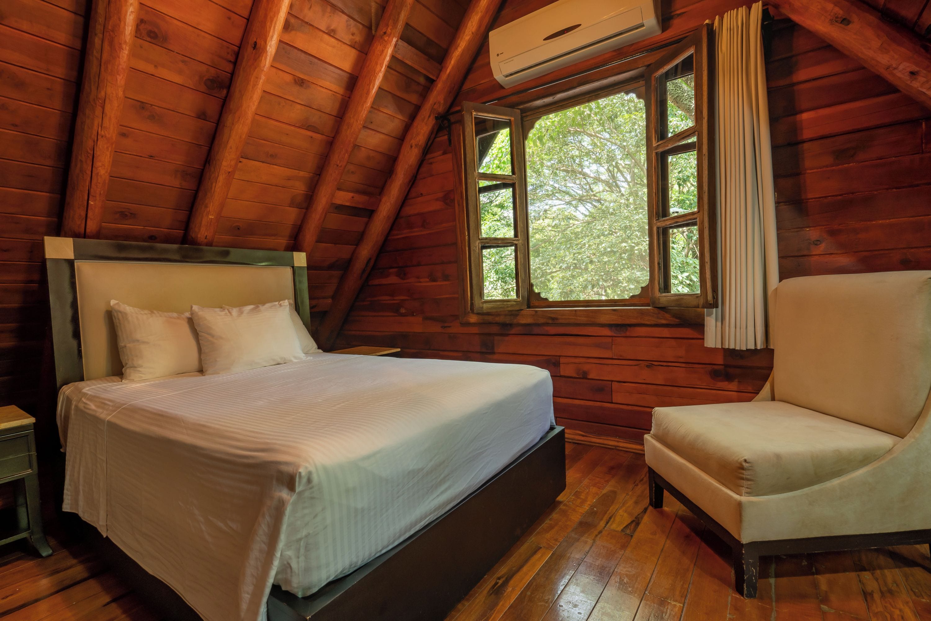 A wooden cabin bedroom with a bed, a chair, and a window with curtains.