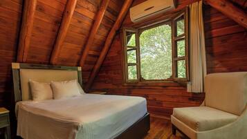 A wooden cabin bedroom with a bed, a chair, and a window with curtains.