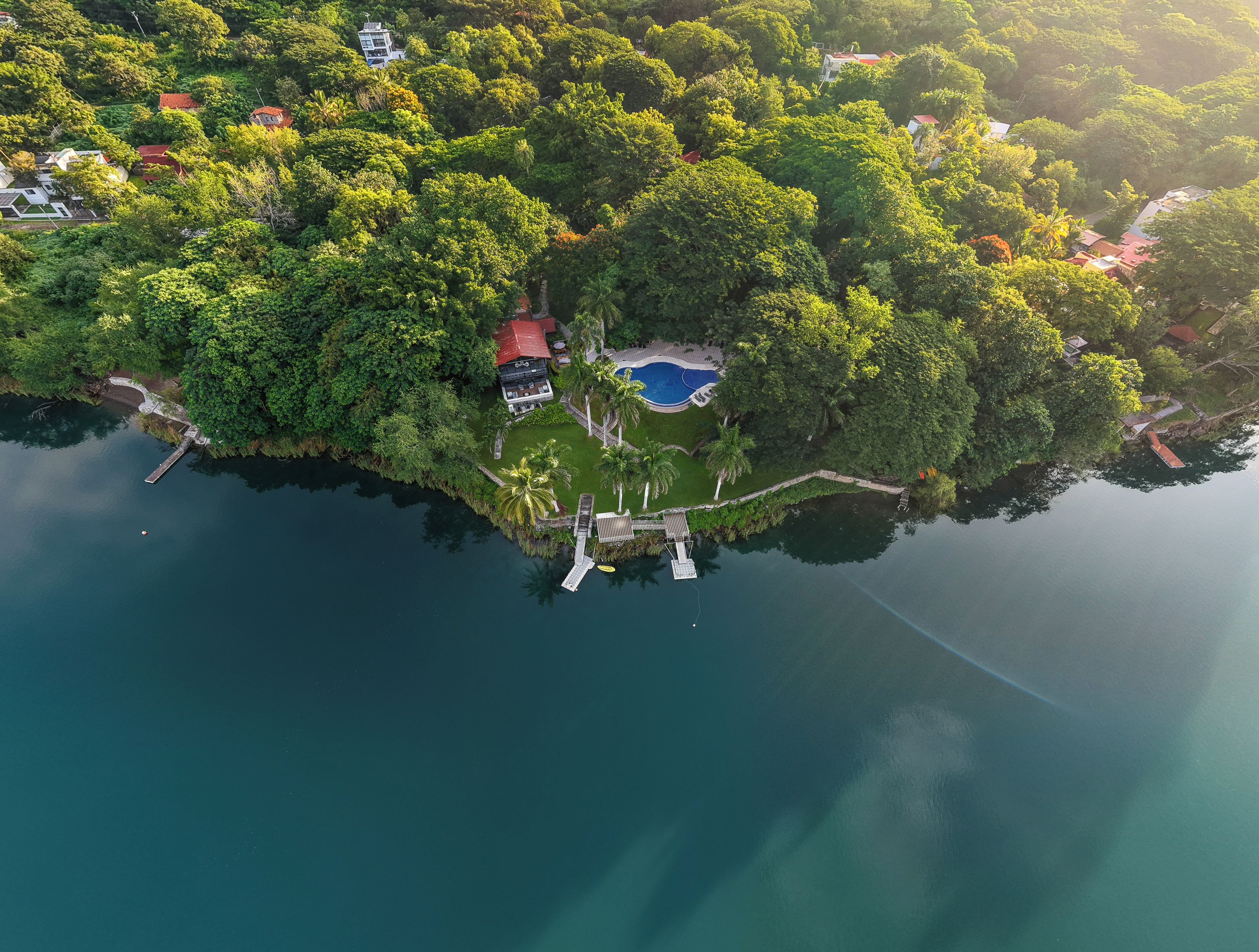 An aerial view of a tropical island with a swimming pool, a dock, and several buildings surrounded by dense greenery.