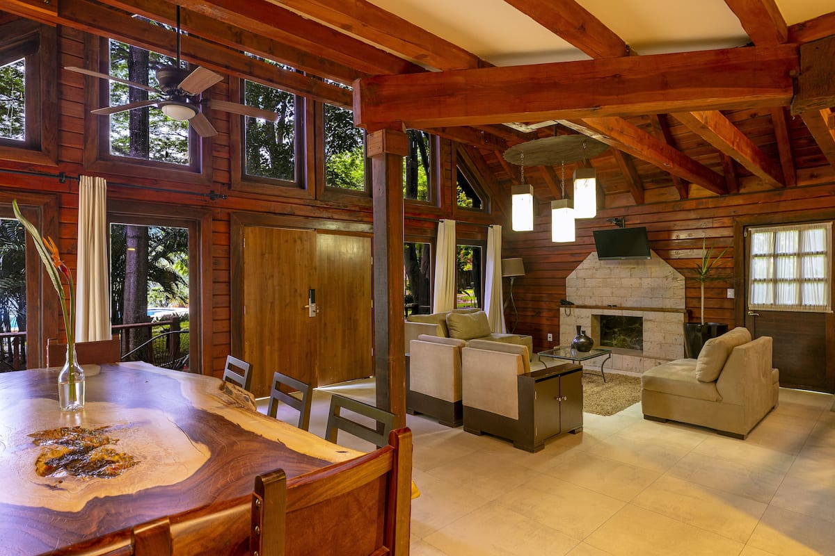 A spacious living area with a fireplace, wooden beams, and large windows.