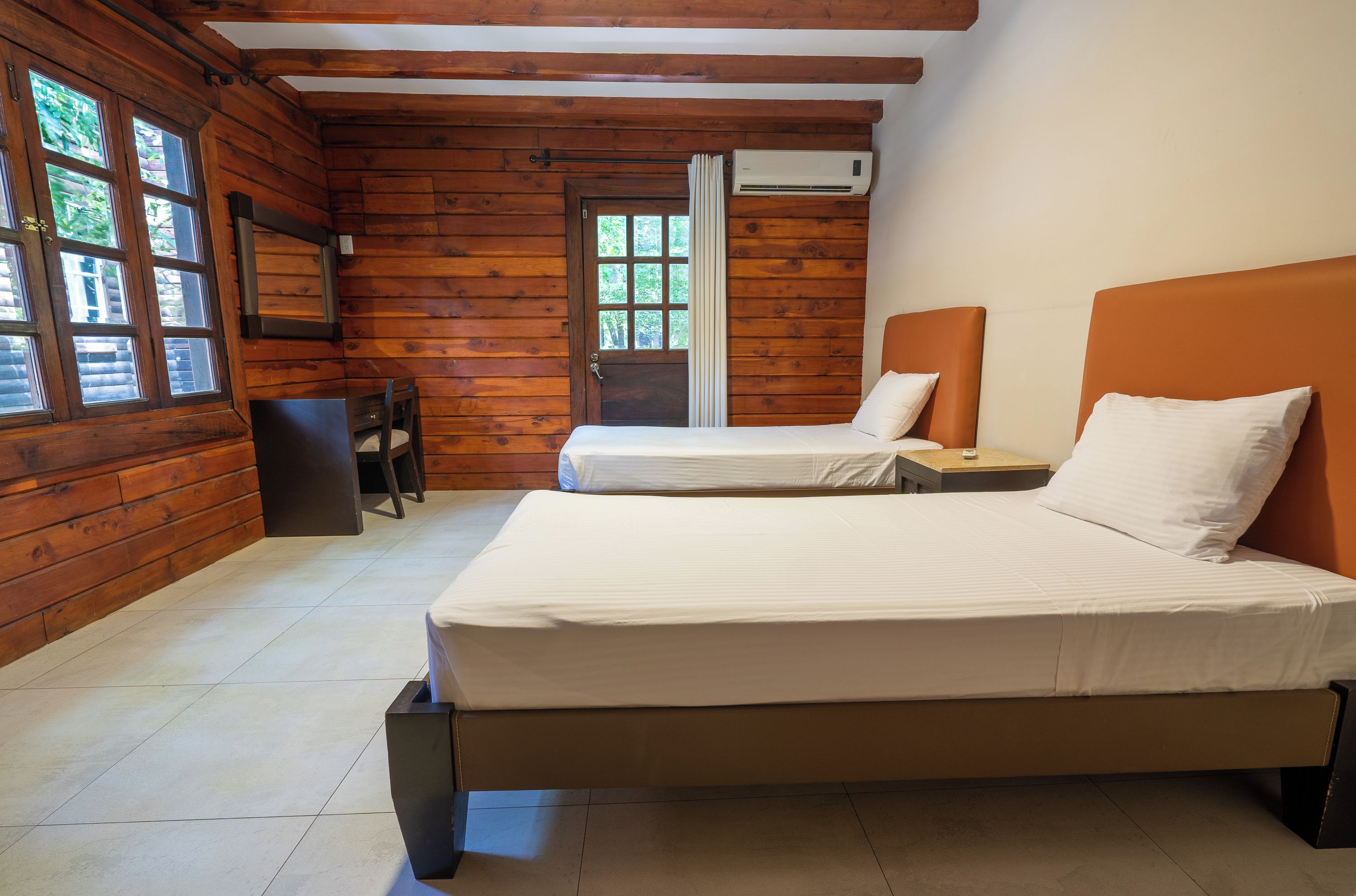 A wooden cabin-style room with two beds, a wooden door, and a window.