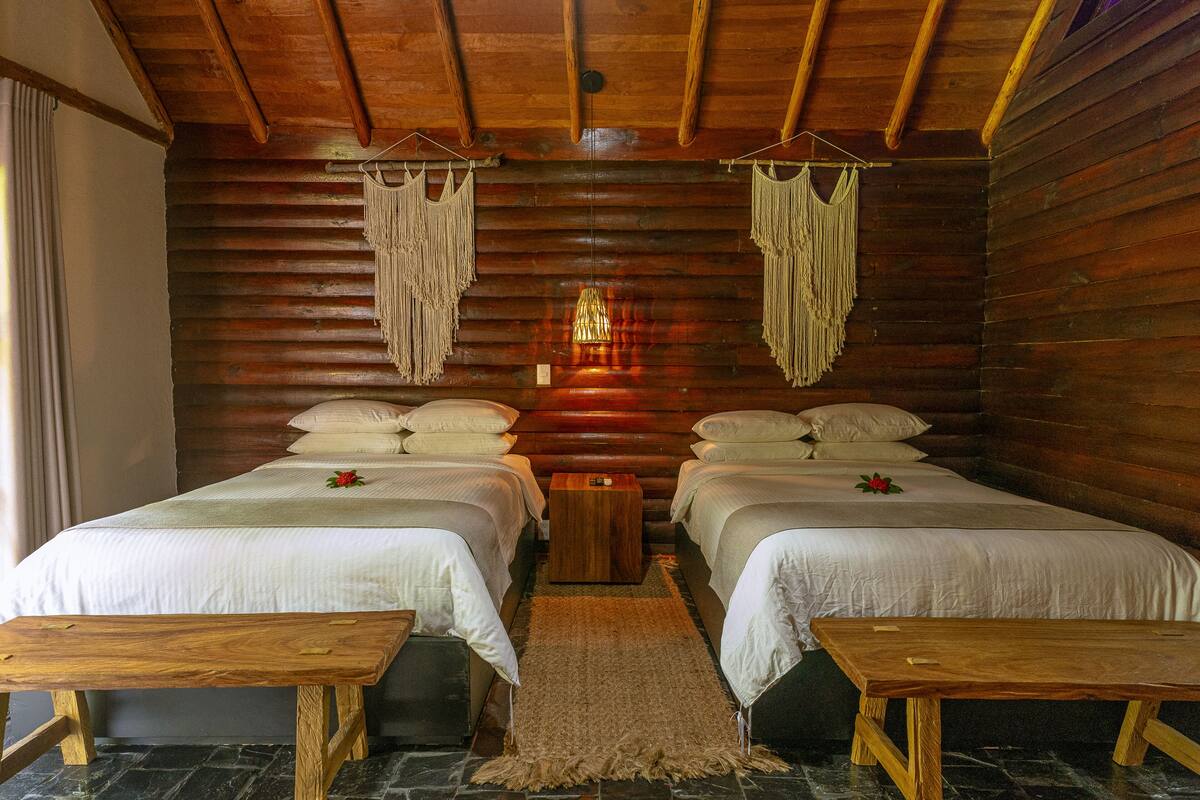 A log cabin-style room with two beds, wooden benches, and macramé wall hangings.