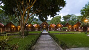 A row of wooden cabins with a central entrance, surrounded by well-maintained lawns and trees. - Santa María Resort (La Laguna)