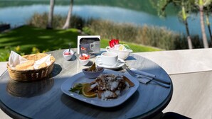 A table with a meal, a basket, and a cup of coffee, overlooking a lake and palm trees. - Santa María Resort (La Laguna)