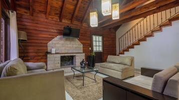A cozy living room with a fireplace, wooden walls, a sofa, a coffee table, and a staircase.