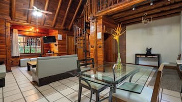 Un interior de madera con una mesa de comedor de vidrio, asientos acolchados y una chimenea.
