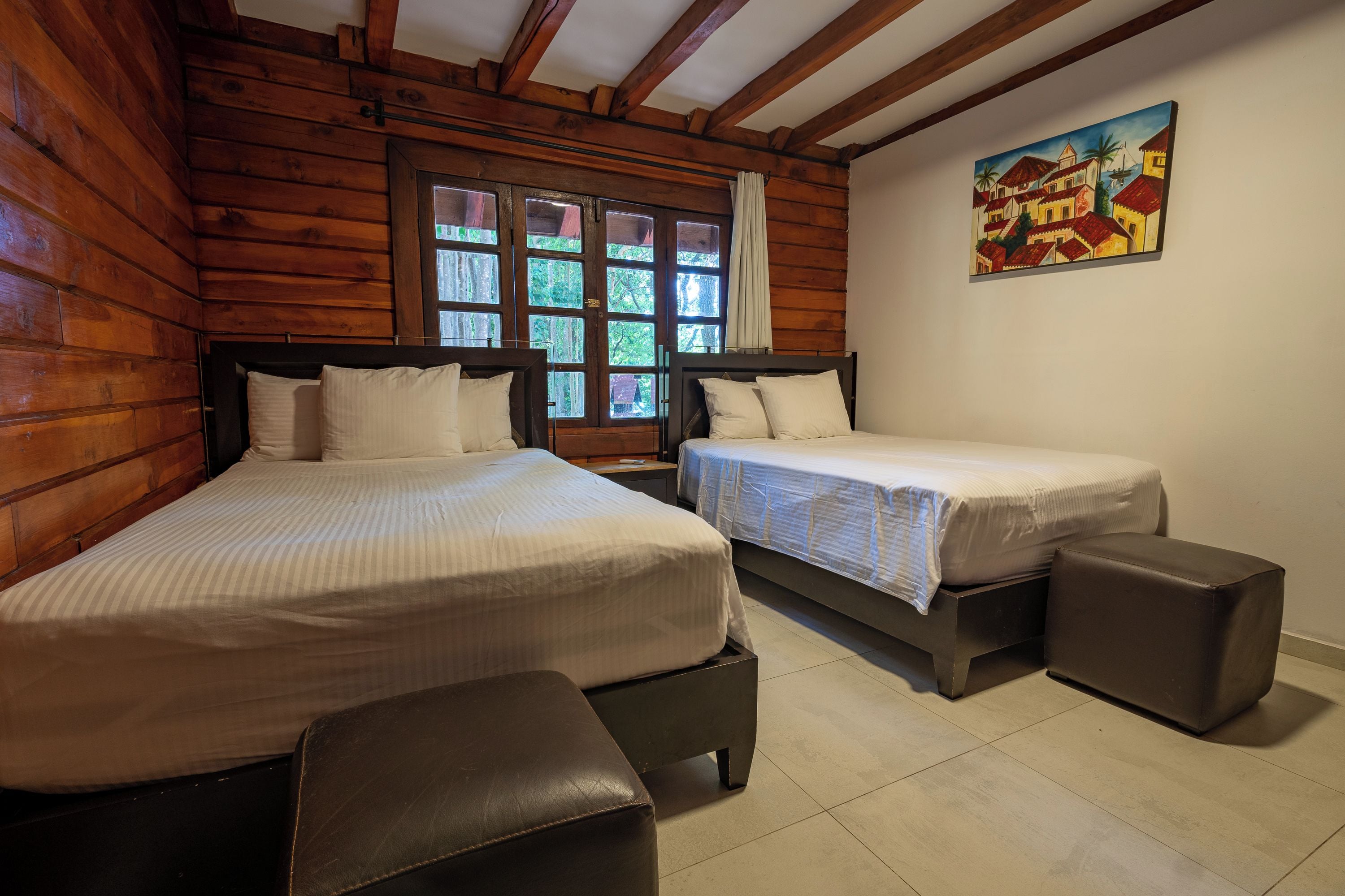 A wooden cabin bedroom with two beds, a window, and a painting on the wall.