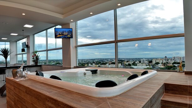 A modern spa area with a large hot tub, large windows offering city views, and a flat-screen TV mounted on the wall. - Porto Minas Hotel e Convenções (Uberlandia)
