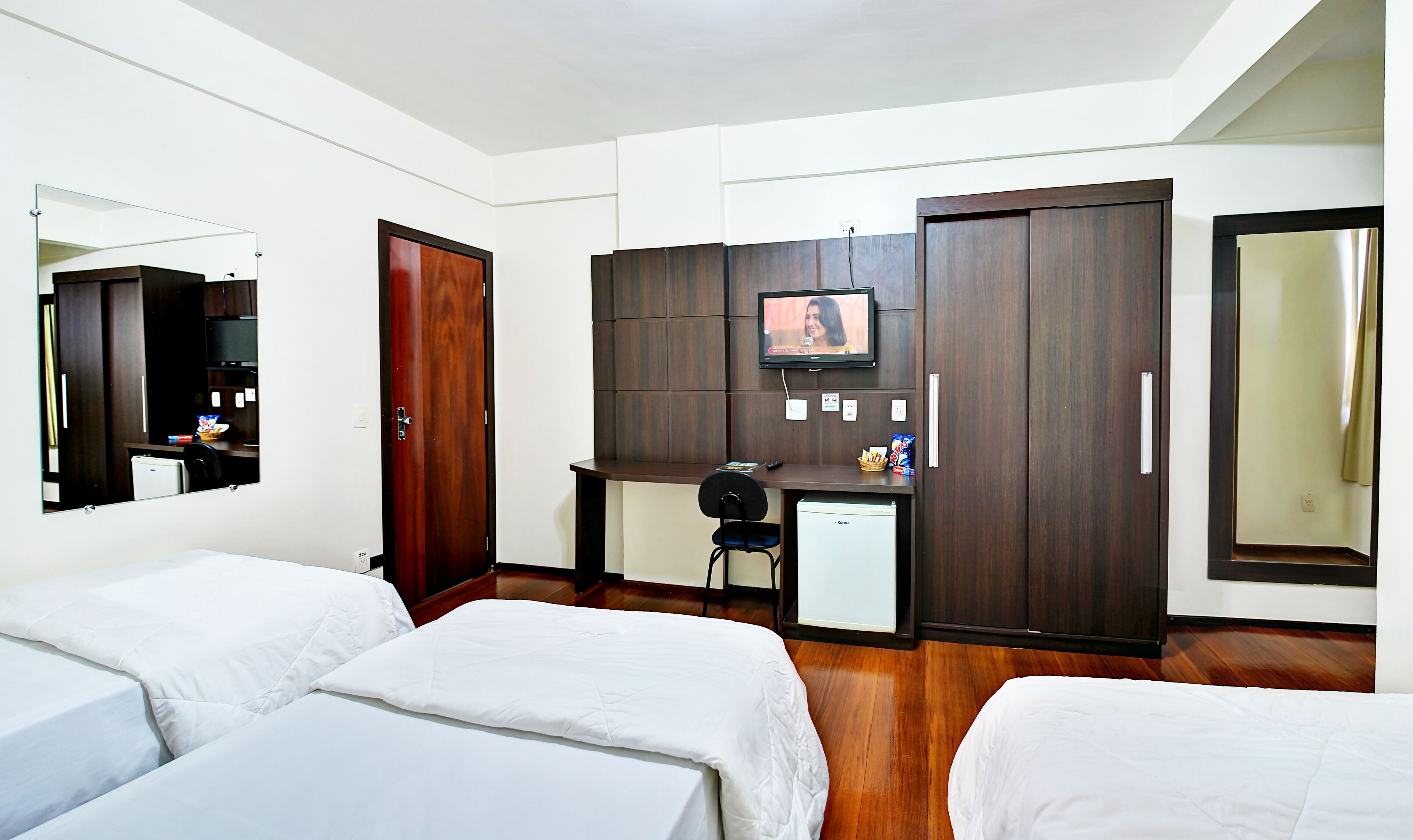 A hotel room with two beds, a desk with a computer, a TV, and a wardrobe.
