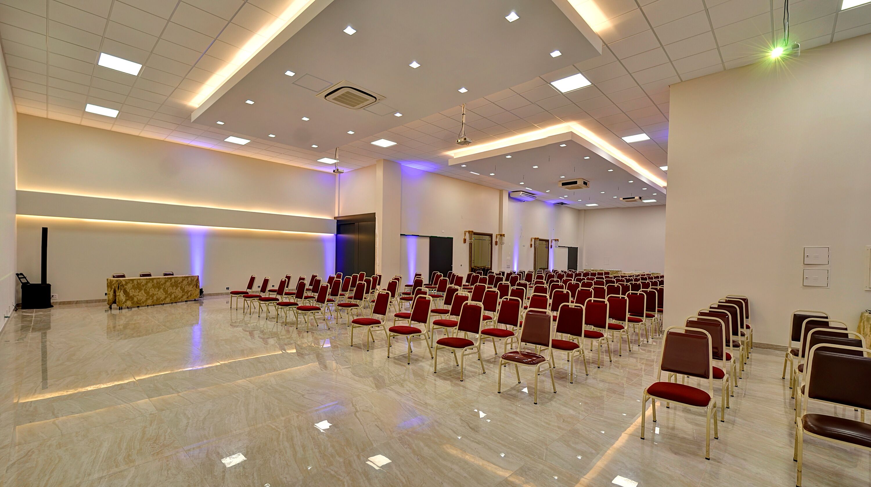 Una grande sala conferenze con file di sedie rosse, un podio e un pavimento in marmo.