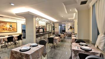 A restaurant with marble flooring, tables set with plates and glasses, and artwork on the walls.