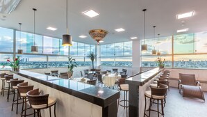A modern bar area with a central island, bar stools, and a view of the cityscape through large windows. - Porto Minas Hotel e Convenções (Uberlandia)