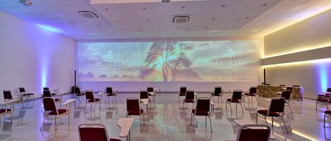 Un salón de conferencias con filas de sillas orientadas hacia una pantalla grande que muestra el nombre y logotipo del hotel.