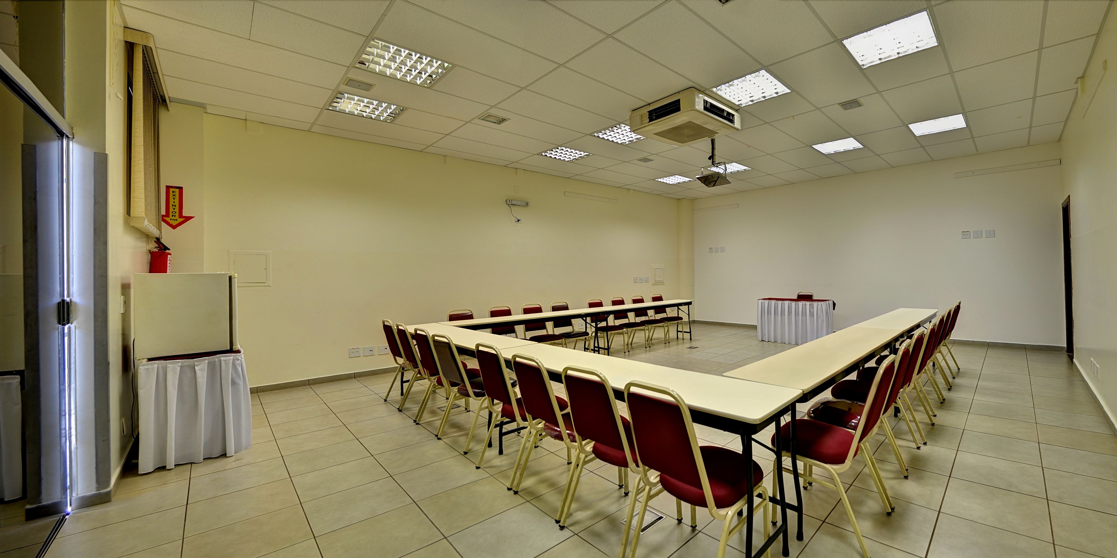 Sala de conferências com uma mesa comprida, cadeiras vermelhas, um projetor e uma lousa.