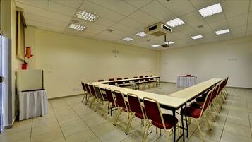 Sala de conferências com uma mesa comprida, cadeiras vermelhas, um projetor e uma lousa.