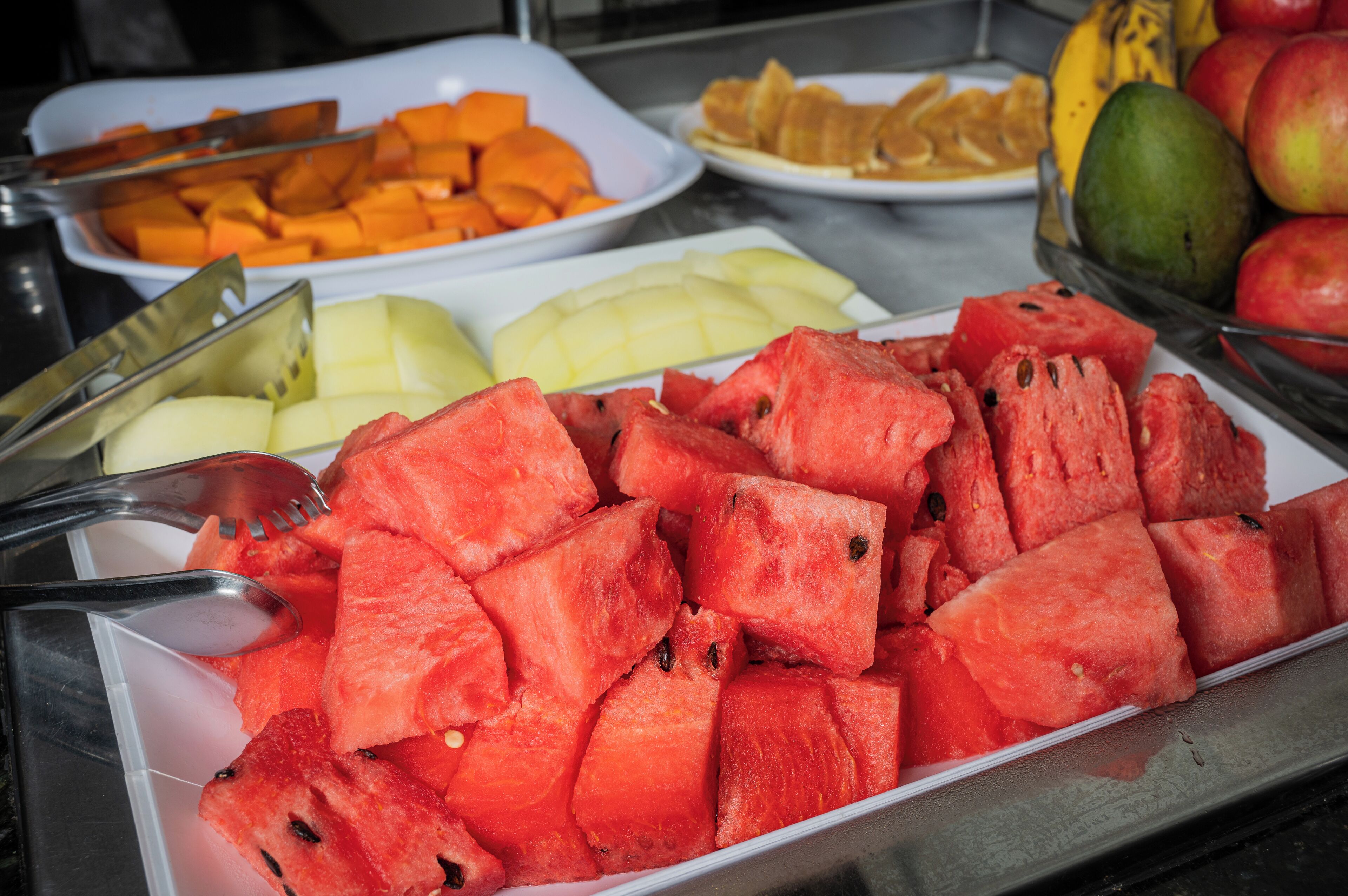 Un bufé con diversas frutas, como sandía, melón y manzanas.