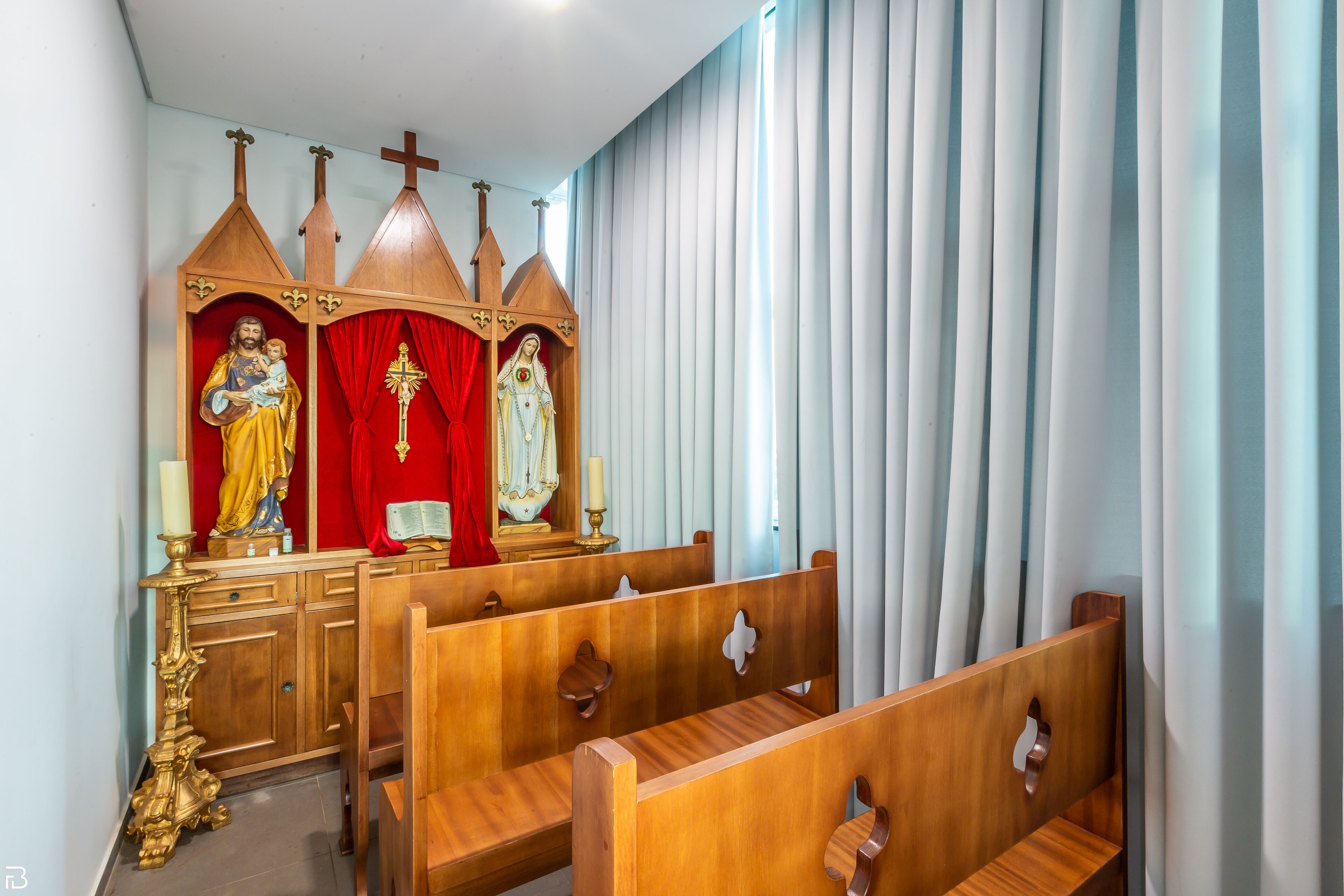 Ein Kircheninneres mit Holzbänken, einem hölzernen Altar mit religiösen Figuren und einem roten Vorhang.