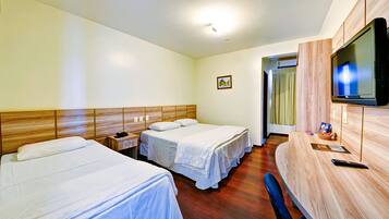 Quarto de hotel com duas camas, uma escrivaninha com televisão e cabeceira de madeira.