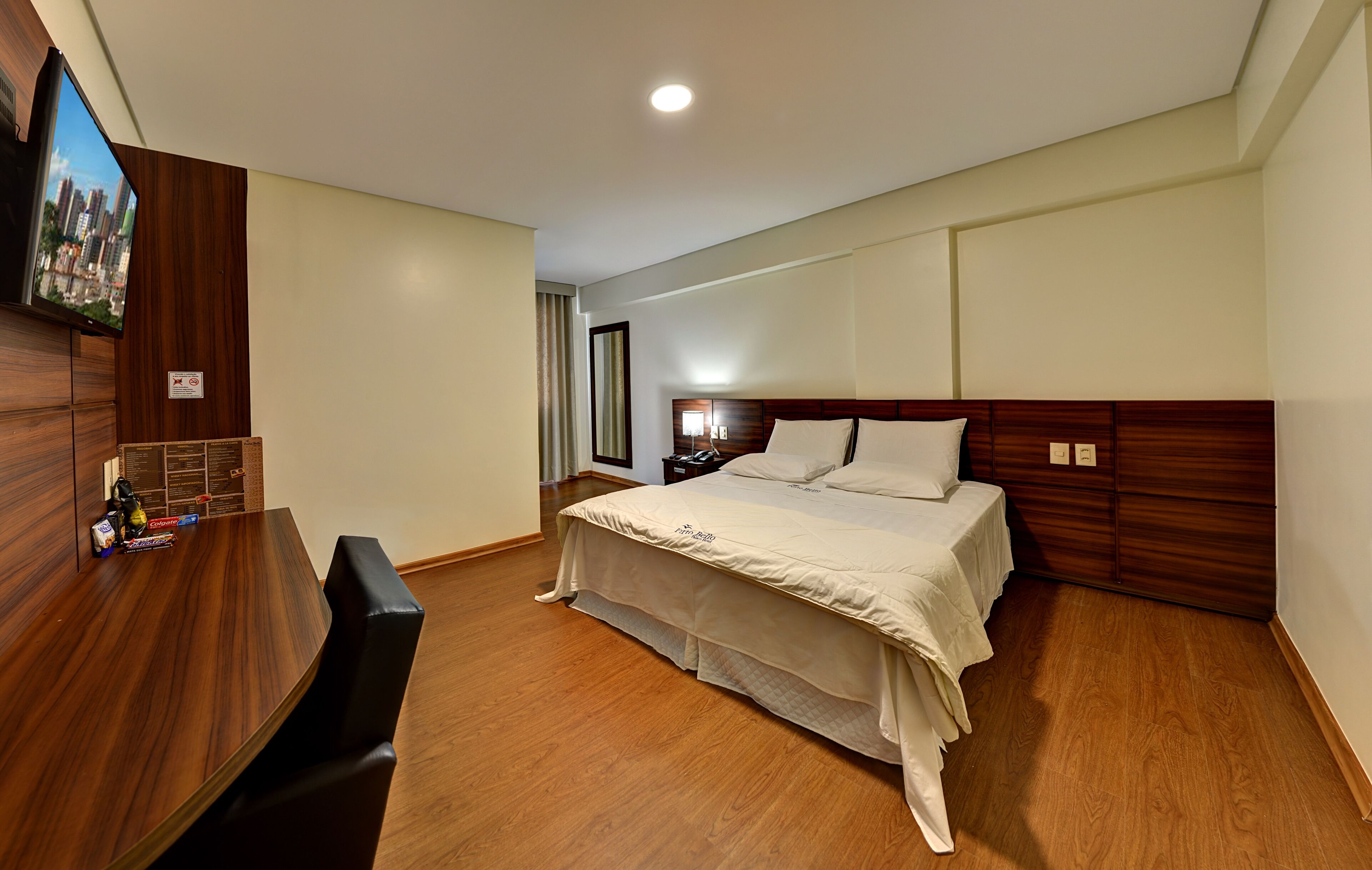 Een hotelkamer met een bed, een bureau en een aan de muur bevestigde televisie.