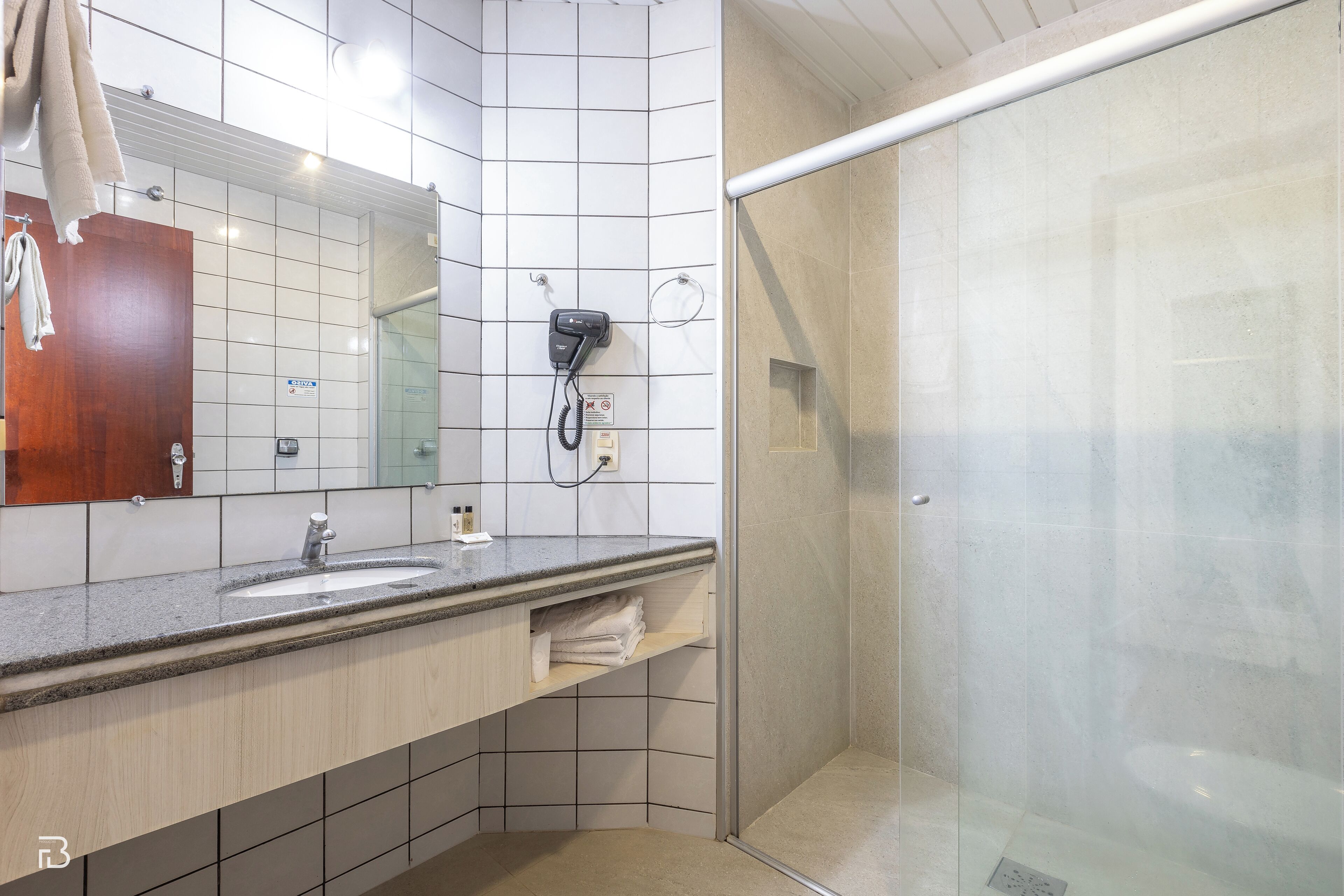 Une salle de bain moderne avec un grand miroir, deux lavabos, un porte-serviettes et une douche séparée par une paroi de verre.
