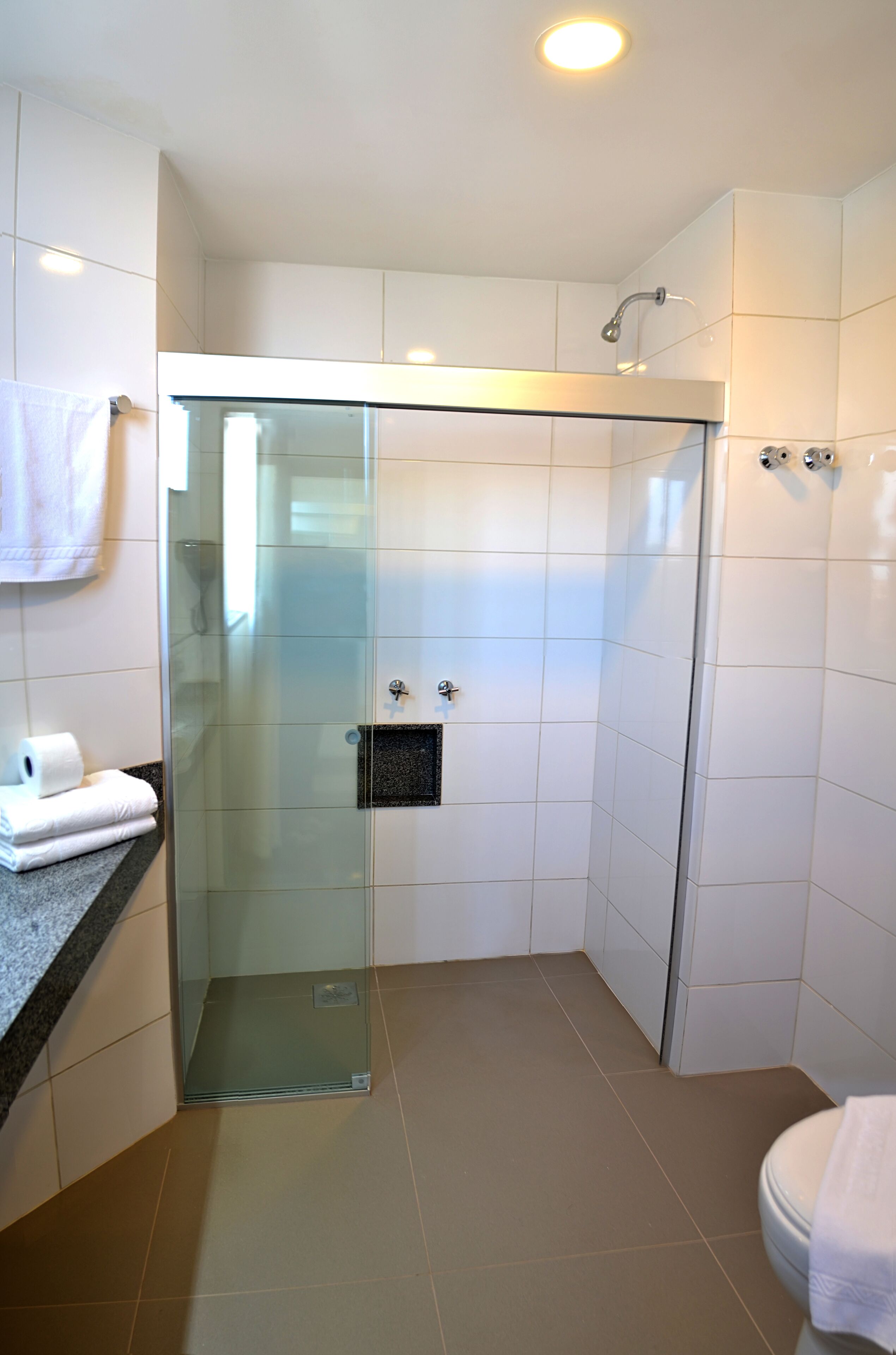 A modern bathroom with a glass-enclosed shower, white tiles, and a granite countertop.