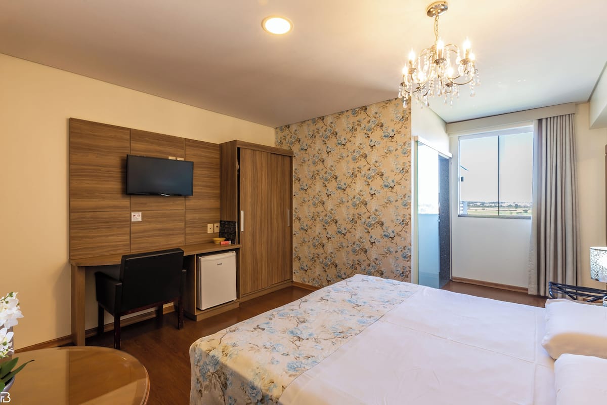 Une chambre d’hôtel équipée d’un lit, d’un bureau, d’une télévision et d’un balcon avec des rideaux.