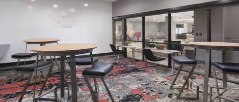 A modern conference room with round tables, black chairs, and a carpeted floor.