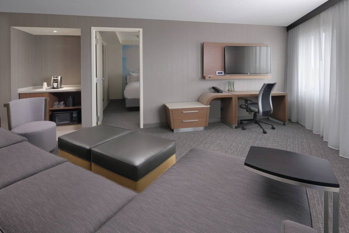 A modern hotel room with a sofa, a desk with a chair, a bed, a TV, and a coffee machine.