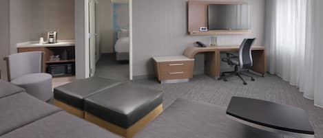 Ein modernes Hotelzimmer mit einer Couch, einem Schreibtisch mit Stuhl, einem Bett, einem Fernseher und einer Kaffeemaschine.