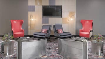 A room with two red chairs, two grey chairs, a TV mounted on the wall, and a patterned carpet.