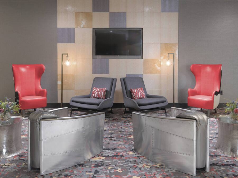 A room with two red chairs, two grey chairs, a TV mounted on the wall, and a patterned carpet.