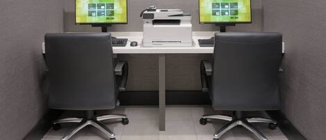 A small office with two desks, each with a computer monitor, keyboard, and mouse. There is a printer on the desk between the two computers.