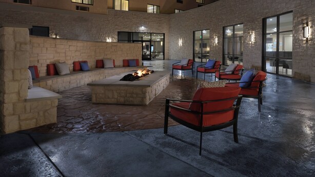 An outdoor seating area with stone walls, a fire feature, and modern chairs. - Courtyard by Marriott Austin Pflugerville and Pflugerville Conference Center (Pflugerville)