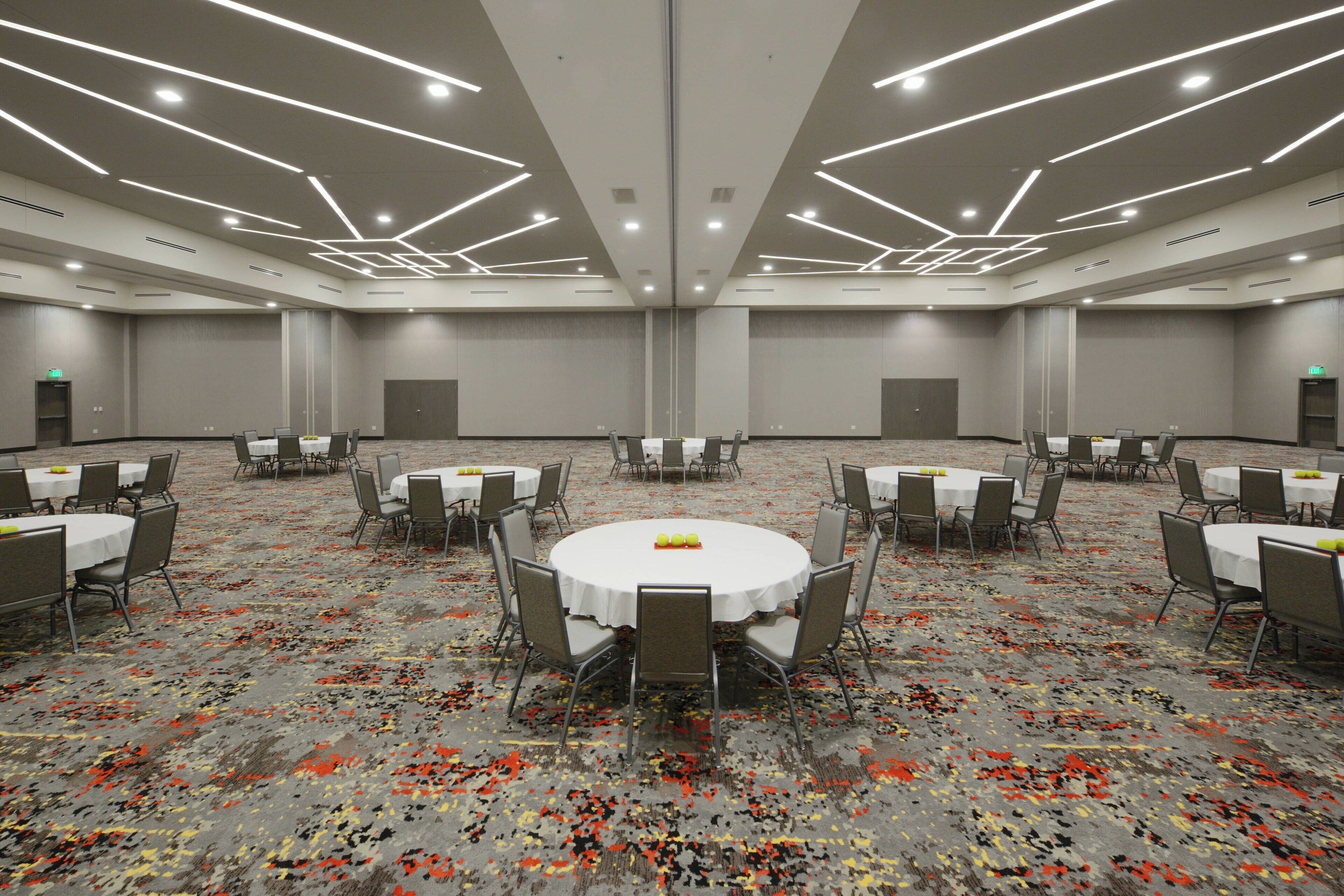 A large conference room with round tables and chairs, equipped with ceiling lights and a carpeted floor.