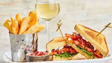 Un sándwich con un palillo, una copa de vino blanco y una cesta de papas fritas sobre un plato.