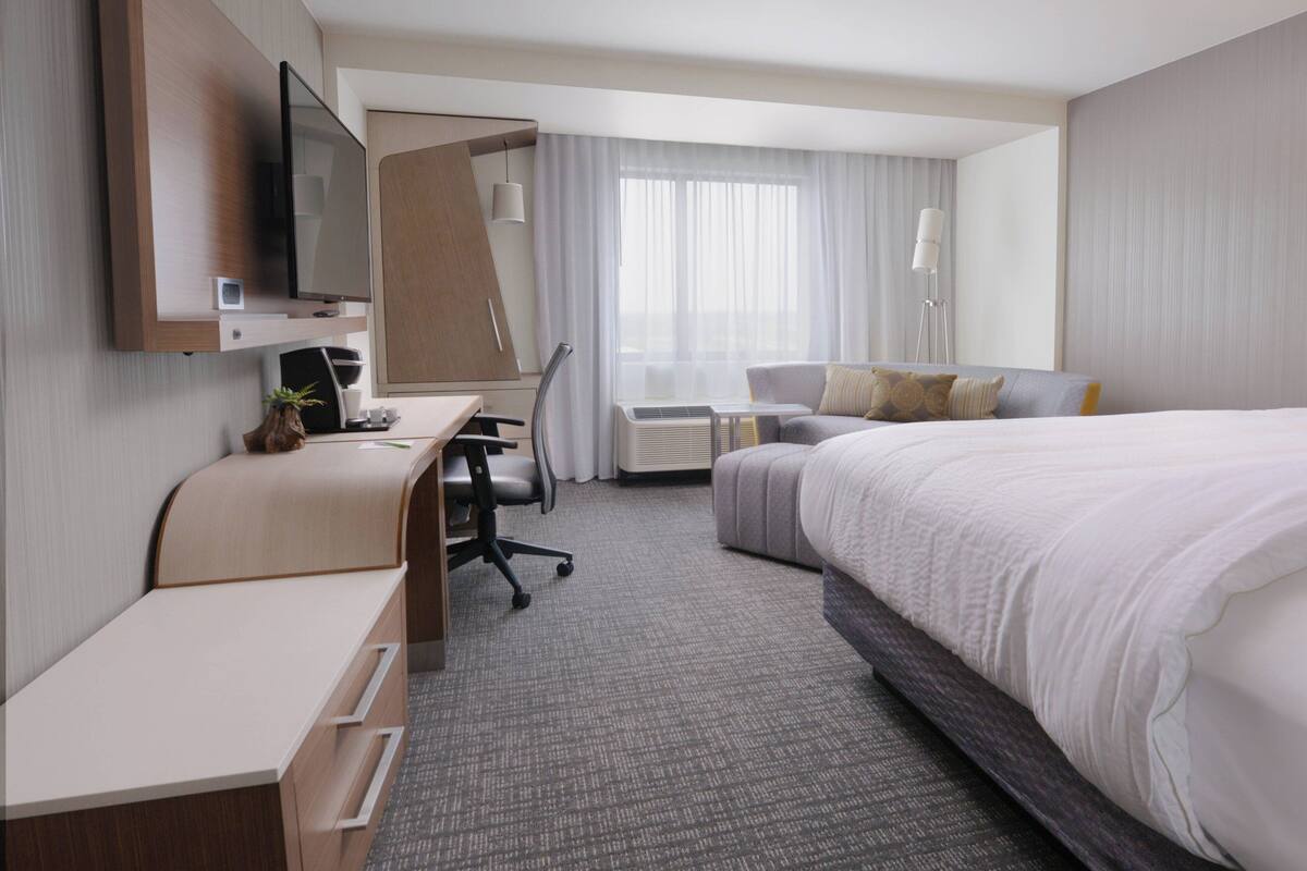A hotel room with a bed, a desk, a chair, a TV, and a window with curtains.