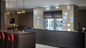 A modern bar area with a dark wood bar counter, red chairs, and a wine display. - Courtyard by Marriott Austin Pflugerville and Pflugerville Conference Center (Pflugerville)