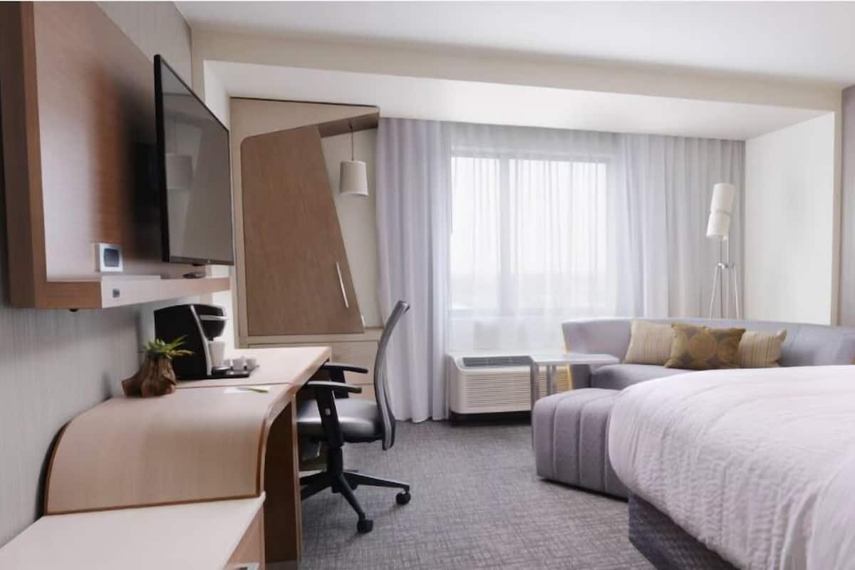 A hotel room with a bed, a desk, a chair, a TV, and a window with curtains.